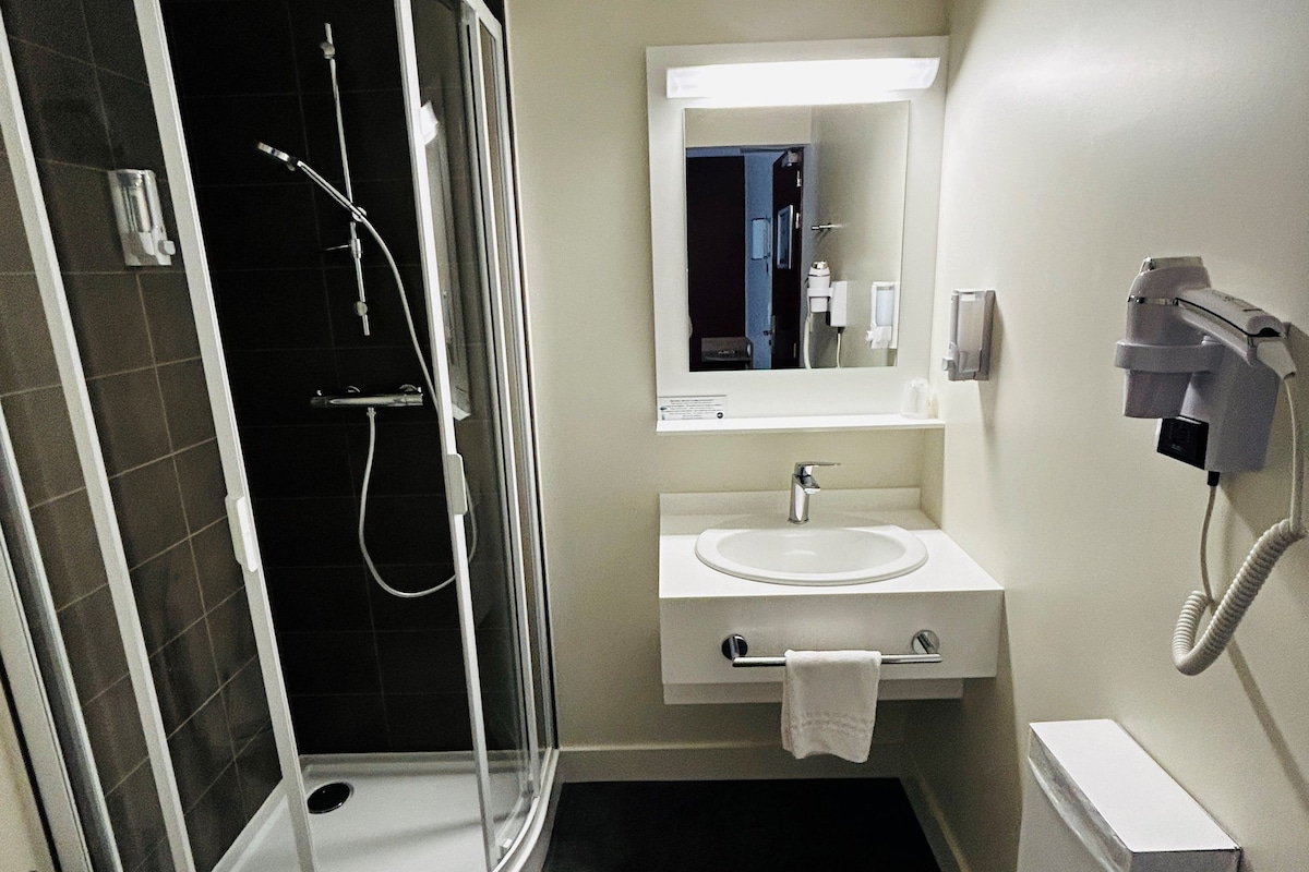 Een moderne badkamer met een douchecabine van glas, een witte wastafel en een spiegel erboven.