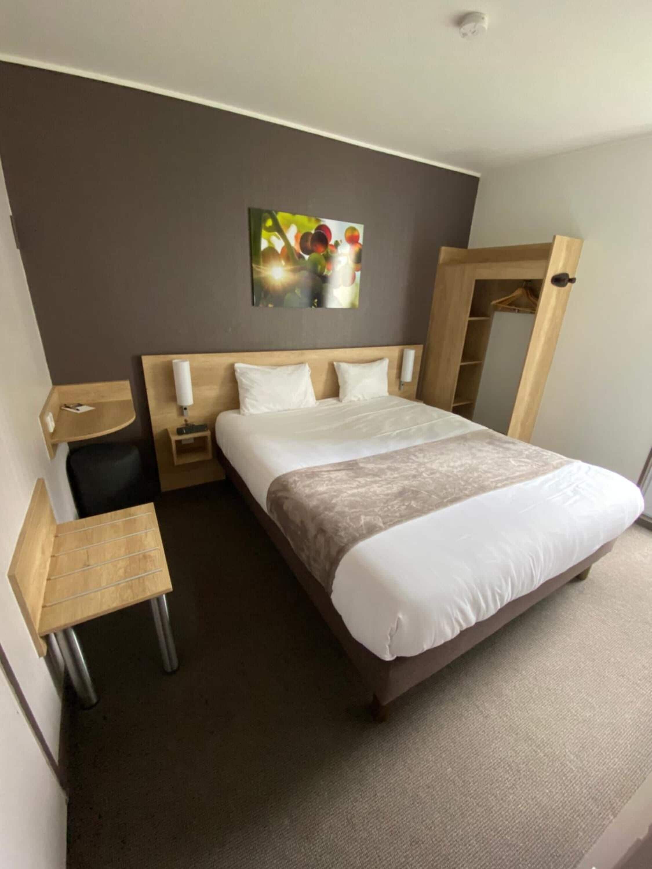 A hotel room with a bed, bedside tables, a desk, a mirror, and a wall-mounted artwork.