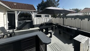 Een achtertuin met een terras, een barbecue, buitenzitplaatsen en een houten omheining.