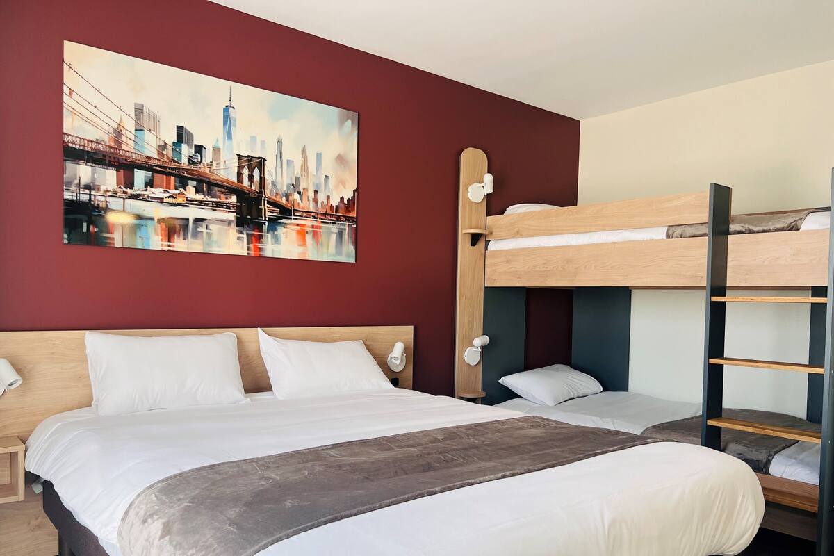 Een hotelkamer met een groot bed, een stapelbed, een stadsgezicht schilderij en een houten hoofdeinde.
