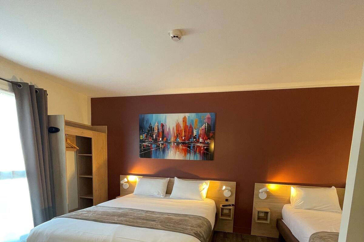 Een hotelkamer met een groot bed, een kleiner bed, een schilderij aan de muur en een houten vloer.
