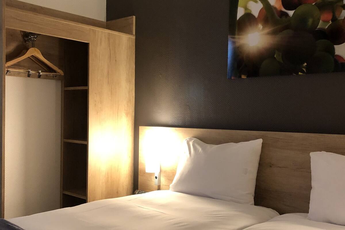 Een hotelkamer met een bed, een houten garderobe, een nachtkastje en een aan de muur hangend schilderij.
