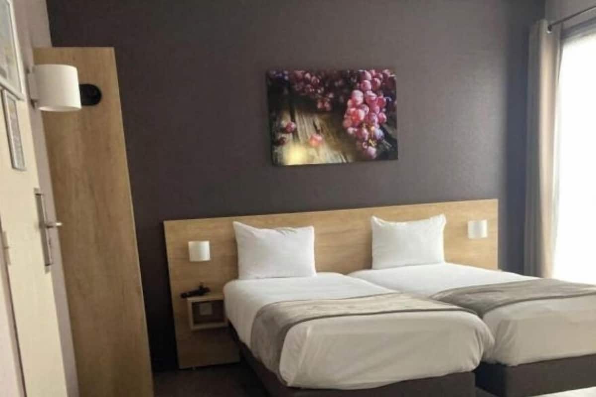 Een hotelkamer met een tweepersoonsbed, een houten hoofdeinde, een nachtkastje en een wandlamp.