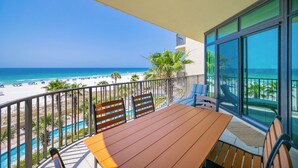 Un balcon avec une table et des chaises en bois, donnant sur une plage et une piscine.