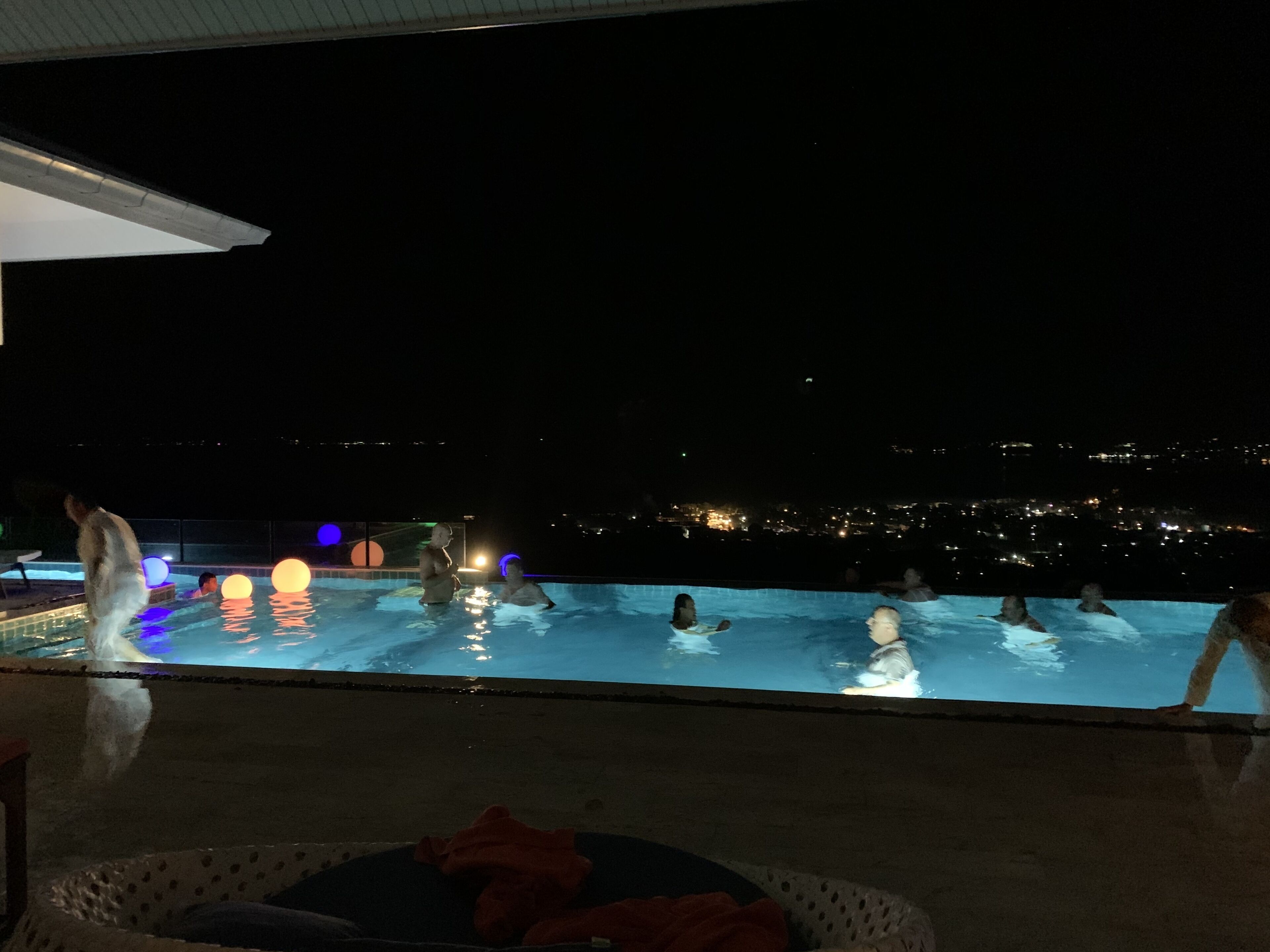 An outdoor swimming pool with people enjoying the water, surrounded by city lights in the background.