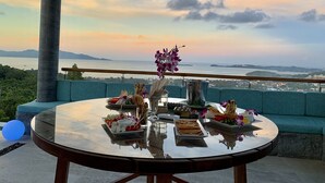 Une table ronde avec de la nourriture et des boissons, un canapé et une vue sur la mer et les montagnes.