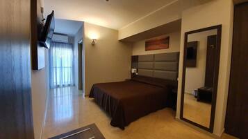 Una habitación de hotel moderna con una cama grande, un televisor de pantalla plana en la pared, un espejo amplio y vistas al pasillo.