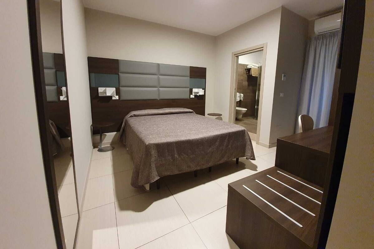 A modern hotel room with a large bed, a desk, and a mirror.