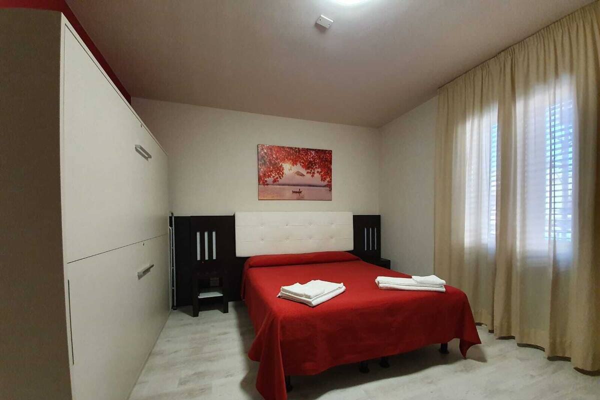 A bedroom with a bed, a painting, a wardrobe, and a window with curtains.
