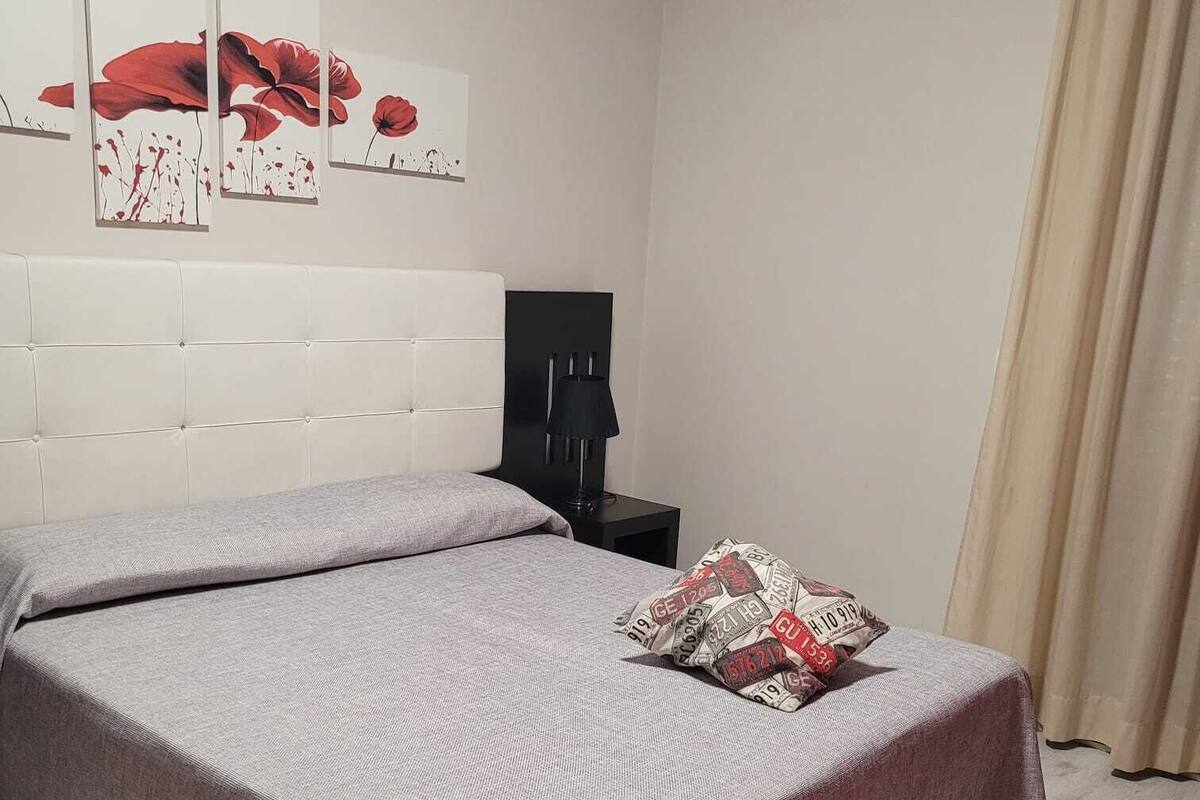 A bedroom with a large bed, a bedside table, a lamp, and a wall-mounted air conditioner.