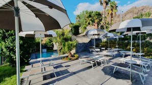 A poolside area with lounge chairs and umbrellas, a pool, and a mountainous backdrop. - Hotel Casale dei Greci (Biancavilla)