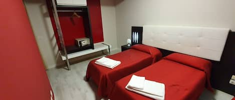 Habitación de hotel con dos camas, una pared roja, un armario y una mesita con una lámpara.