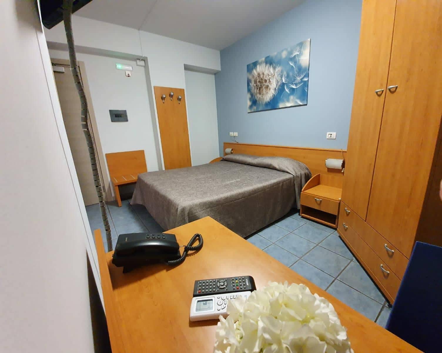 Ein Hotelzimmer mit Bett, Schreibtisch mit Telefon und Fernbedienung, einem Holzschrank und einem Bild an der Wand.