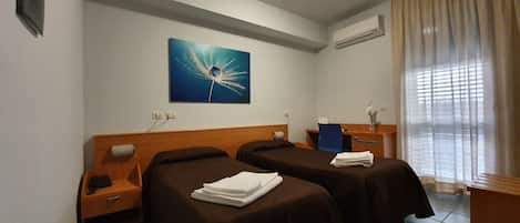 Habitación de hotel con dos camas, un escritorio, una silla, un cuadro y un equipo de aire acondicionado.