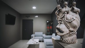 A modern interior with a decorative head sculpture on a table, a sofa, and a coffee table in the foreground. - Hotel Casale dei Greci (Biancavilla)