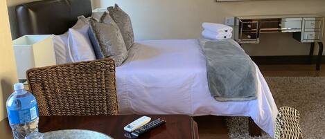 A hotel room with a bed, bedside table, chair, and a desk with a mirror.
