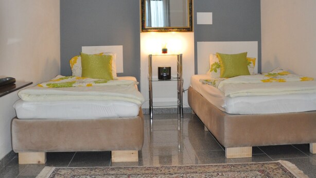 A hotel room with two beds, a large mirror, a nightstand, and a patterned rug. - Appartment Graz Zentrum (Graz)