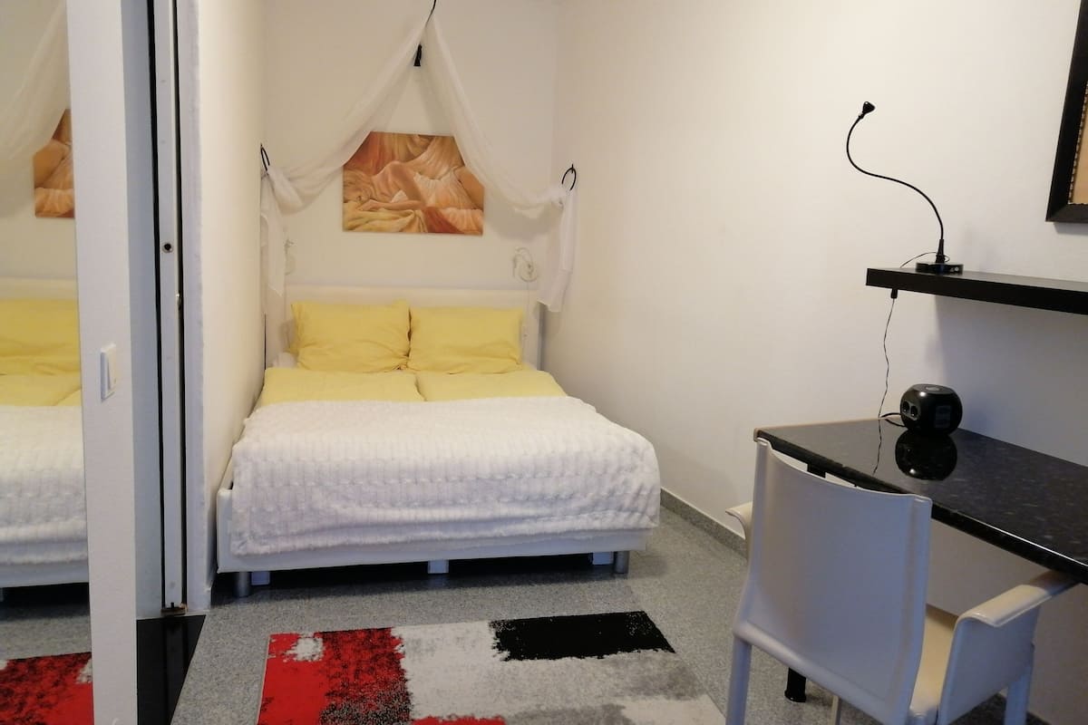 A bedroom with two beds, a desk, a chair, a computer, and a painting on the wall.