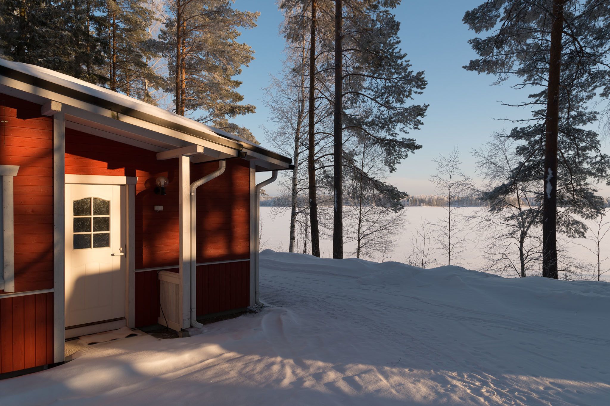 A cabin with a wooden exterior, a white door, and a view of a snowy landscape with trees.