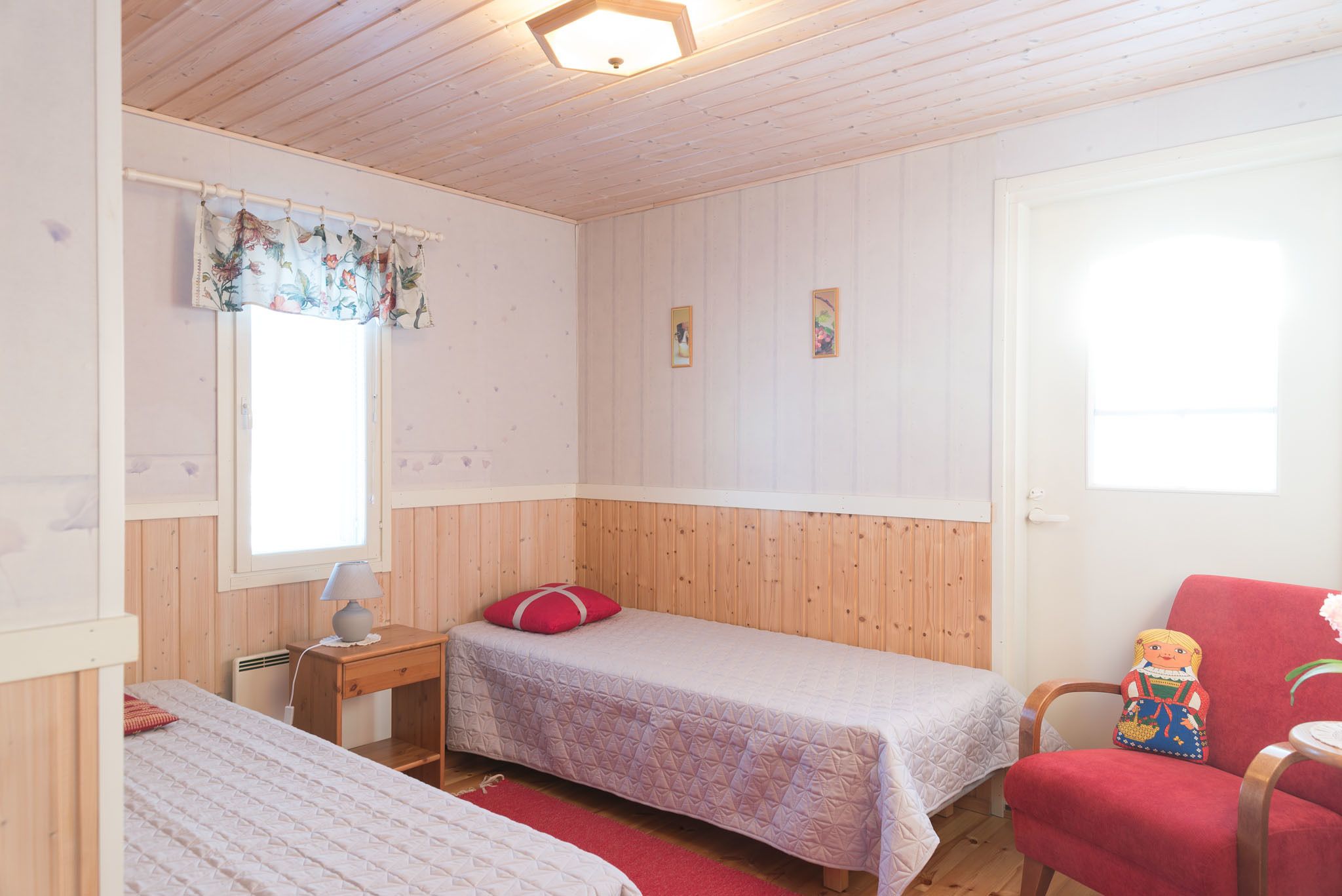A room with two beds, a wooden desk, a chair, and a window with a curtain.