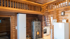 Ein Holzblockhaus-Interieur mit Kamin aus Stein, Holzbalken und einem weißen Kühlschrank.