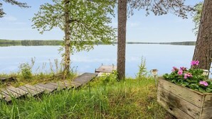 Eine Holzstege führt zu einem stillen See, umgeben von Bäumen und einem Blumenbeet.