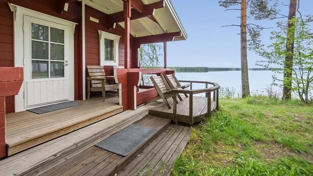 Eine Holzterrasse mit überdachter Sitzgelegenheit, einer Tür und Blick auf einen See.