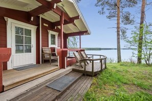 Een houten terras met een overdekte zithoek, een deur en uitzicht op een meer.