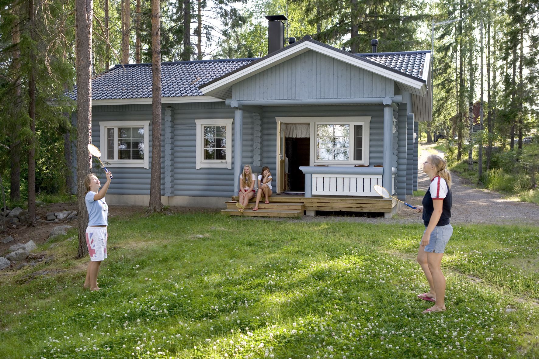 A log cabin with a porch, surrounded by trees.