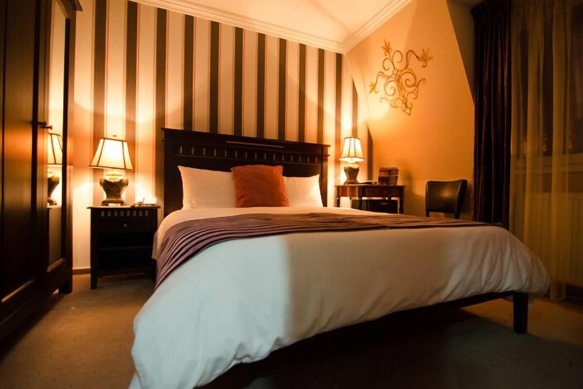 A hotel room with a large bed, two bedside tables with lamps, a chair, and a decorative wall piece.