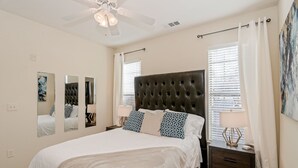 A bedroom with a tufted headboard, a large bed with patterned pillows, a nightstand with a lamp, and a ceiling fan.