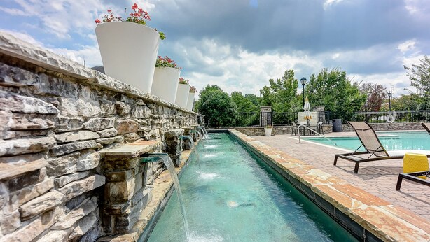 A stone-lined pool with a clear blue water feature, surrounded by lounge chairs and potted plants.