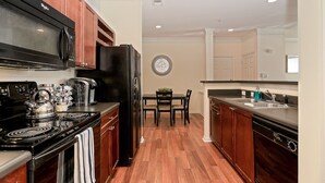 A compact kitchen with a microwave, stove, refrigerator, and a dining area with chairs and a table.