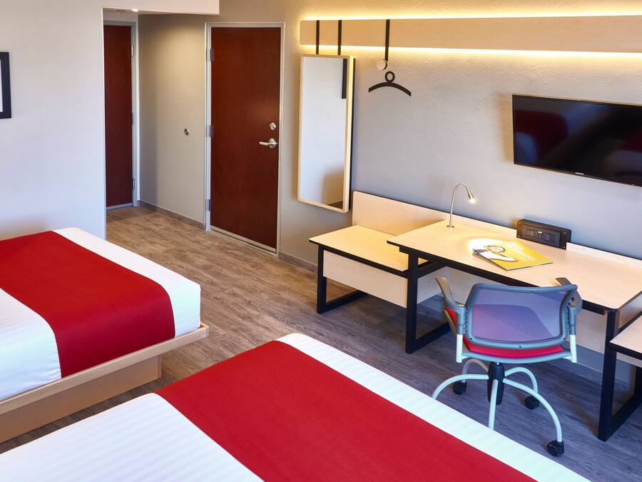 Habitación de hotel con dos camas, un escritorio, una silla, un televisor y un espejo.