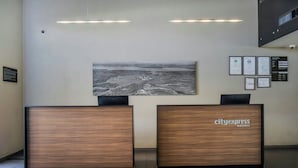 Un mostrador de recepción con una obra de arte urbana, certificados enmarcados y el letrero 'cityexpress hotels'.
