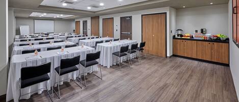 A conference room with multiple tables, chairs, and a kitchenette area.
