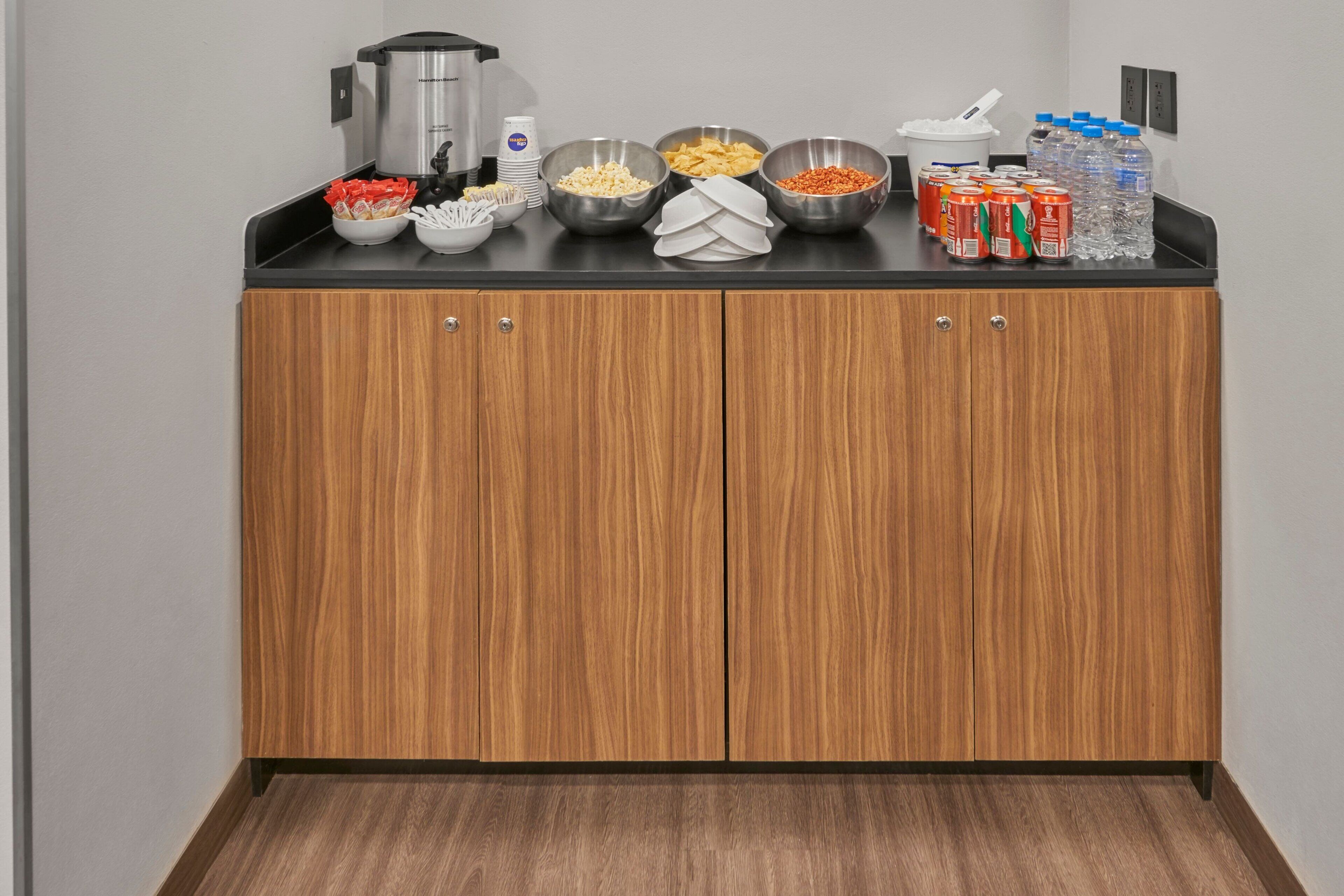 A kitchenette with a coffee maker, bowls of food, and bottled water.