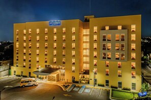 A multi-story hotel with a prominent 'City Express by Marriott' sign, a covered parking area, and a clear view of the surrounding cityscape. - City Express by Marriott Tepic (Tepic)