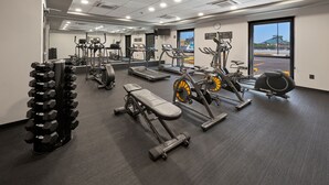 Un gimnasio con máquinas de cardio, bancos de pesas y un espejo grande.