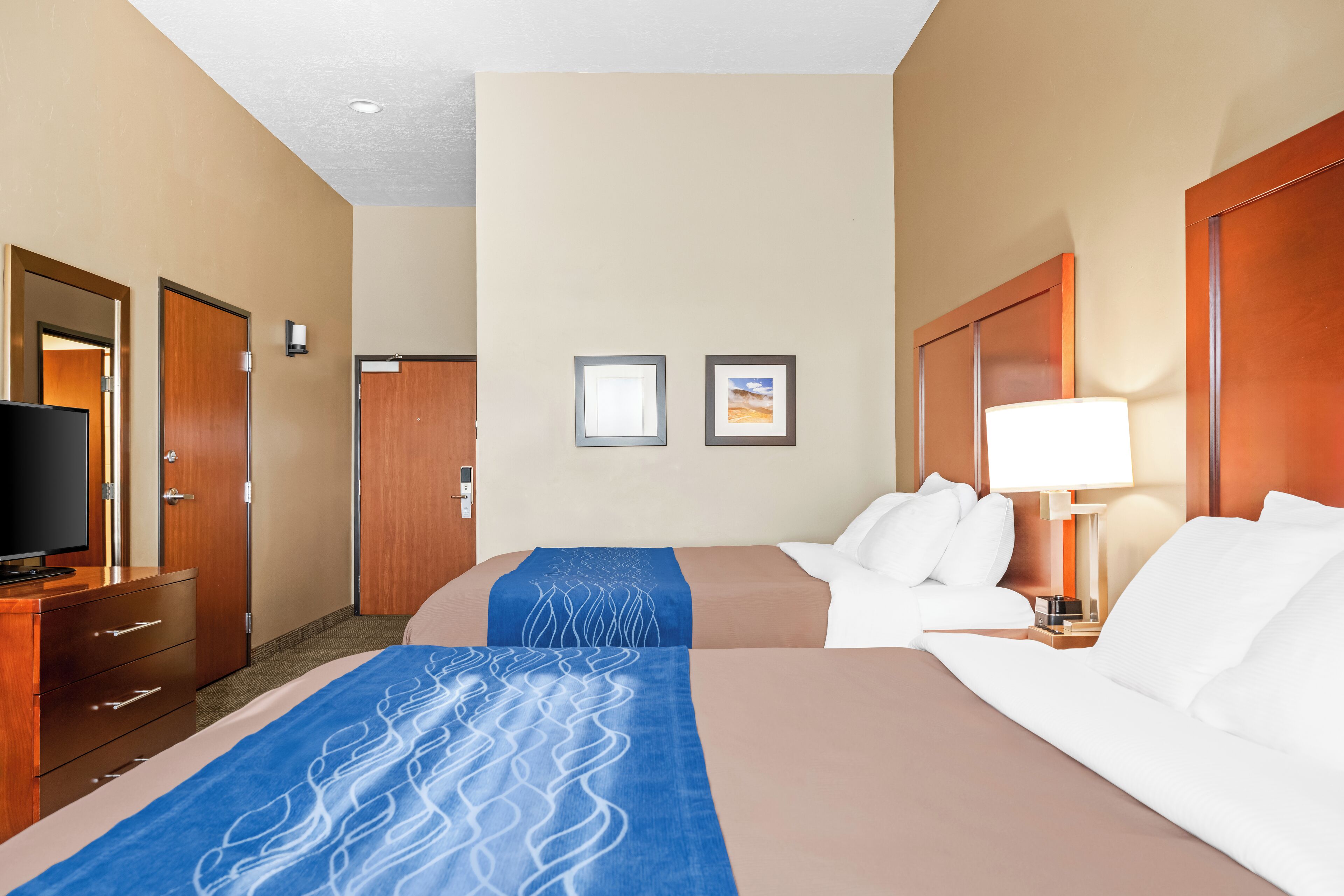 A hotel room with two beds, a television, a desk, and a nightstand with a lamp.
