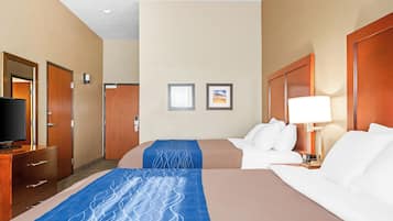A hotel room with two beds, a television, a desk, and a nightstand with a lamp.