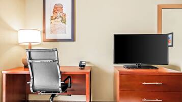 Habitación de hotel con escritorio, silla, televisor y un cuadro en la pared.