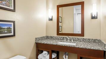 A bathroom with a granite countertop sink, a wooden vanity, a toilet, and two framed pictures on the wall.