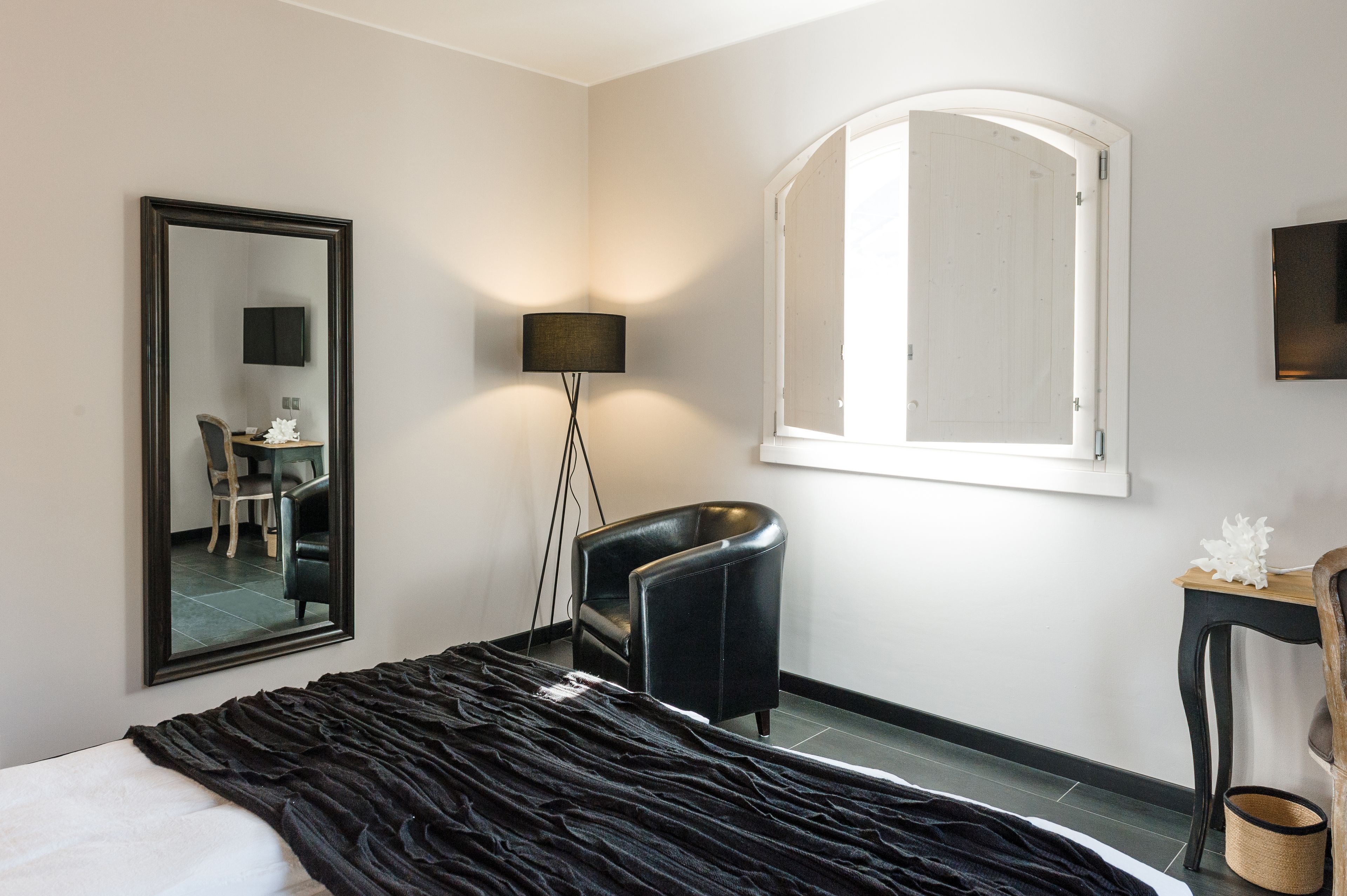 A hotel room with a bed, a desk, a chair, a lamp, and a large mirror.