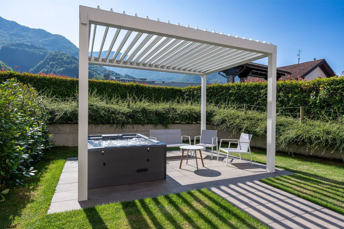 Un espace extérieur aménagé, abrité et doté d’un jacuzzi, de chaises et d’une table, entouré d’une haie bien entretenue et offrant une vue sur les montagnes.