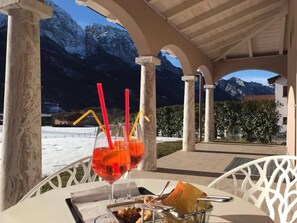 A table with a drink, snacks, and a view of snow-covered mountains. - Bianco Hotel (Primaluna)