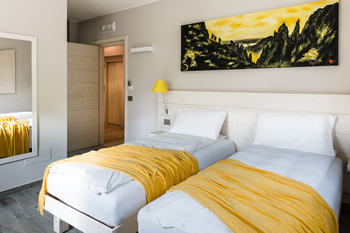 Une chambre d’hôtel avec deux lits, un tableau au mur et une fenêtre donnant sur l’extérieur.