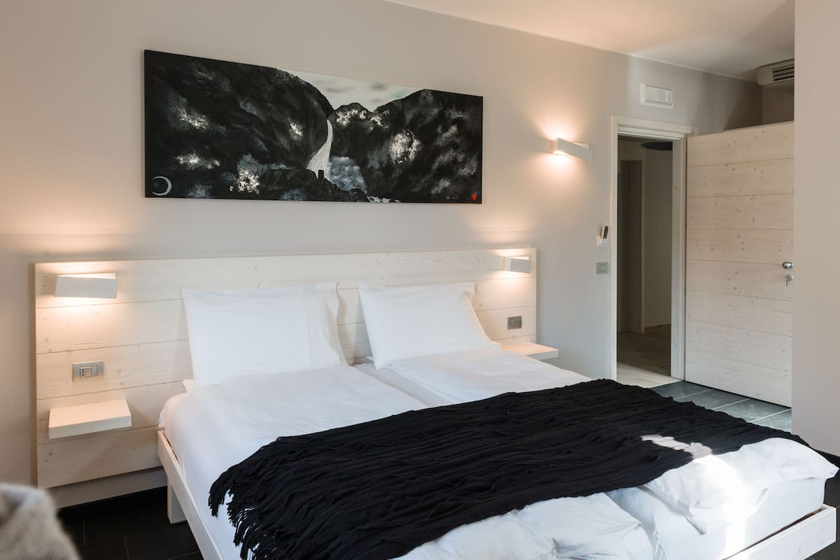 Une chambre à coucher moderne avec un grand lit, des tables de chevet, une armoire et une œuvre d’art accrochée au mur.