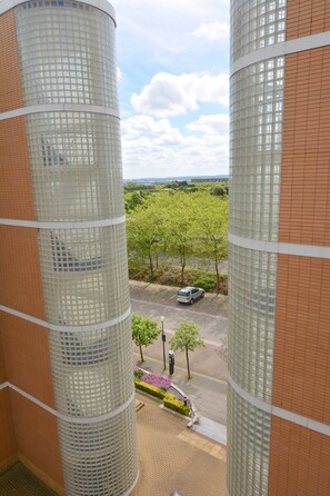 A view from inside a building looking out at a parking area with trees and a car. - Brightleap Apartments - Silbury View (Milton Keynes)