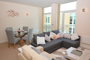 Uma sala de estar moderna com um sofá seccional, uma mesa de jantar com cadeiras e uma grande janela com vista para a cidade.